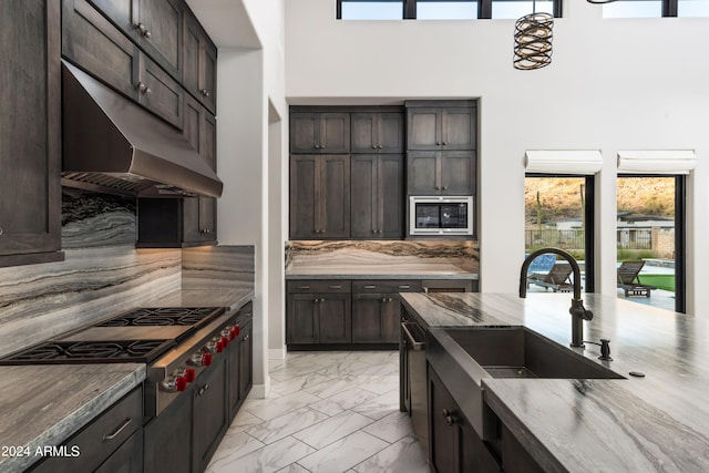 kitchen with marble finish floor, stainless steel appliances, a sink, dark stone countertops, and under cabinet range hood