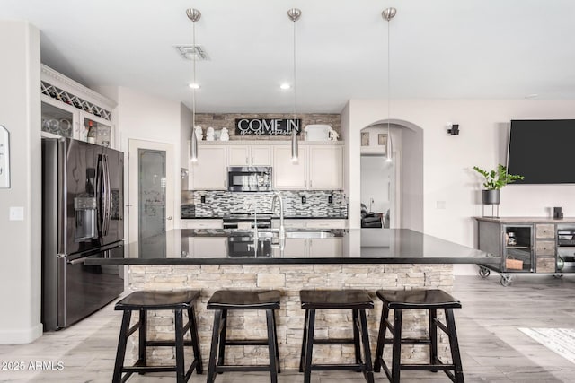 kitchen with fridge with ice dispenser, a breakfast bar area, an island with sink, pendant lighting, and white cabinets