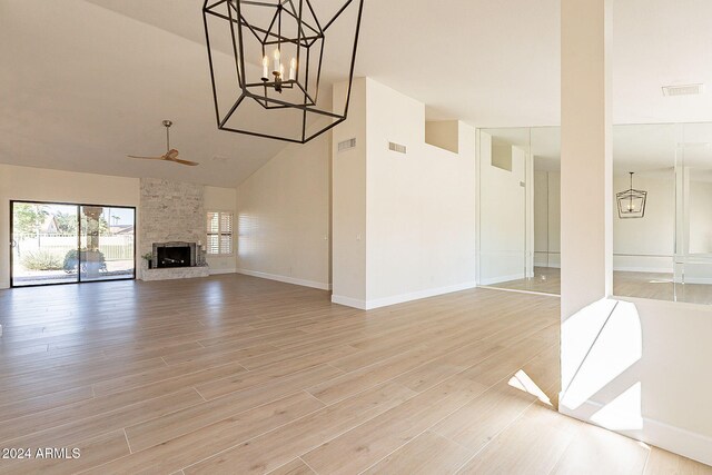 unfurnished living room with high vaulted ceiling, light wood finished floors, a chandelier, ceiling fan, and a large fireplace