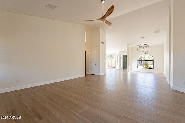 unfurnished living room with a chandelier, a ceiling fan, wood finished floors, high vaulted ceiling, and baseboards