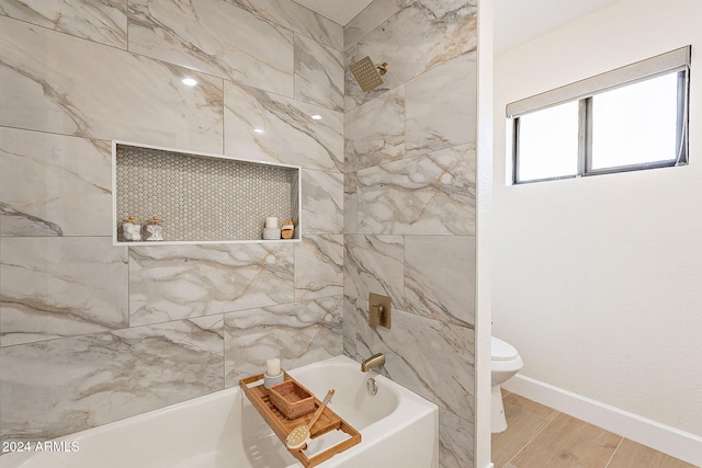 bathroom featuring toilet, wood finished floors, washtub / shower combination, and baseboards