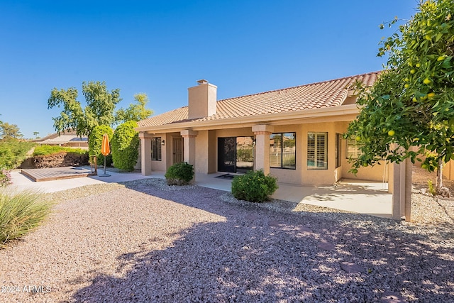 back of house with a chimney, a patio, stucco siding, and a tiled roof