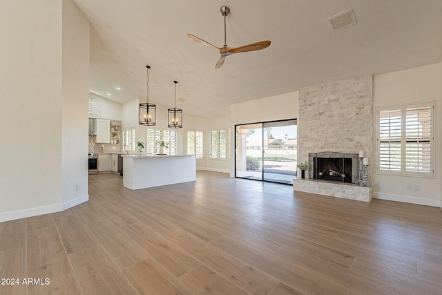 unfurnished living room with a ceiling fan, a stone fireplace, baseboards, light wood finished floors, and high vaulted ceiling