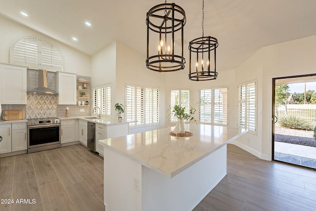 kitchen with wall chimney exhaust hood, appliances with stainless steel finishes, open shelves, a sink, and a chandelier