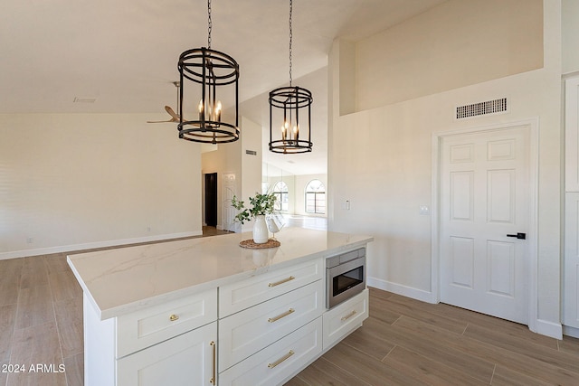 kitchen featuring light hardwood / wood-style floors, stainless steel microwave, light stone countertops, white cabinetry, and decorative light fixtures