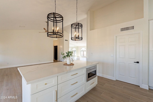 kitchen featuring stainless steel microwave, high vaulted ceiling, a chandelier, light wood-style flooring, and white cabinetry
