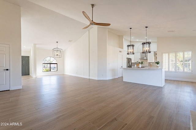 unfurnished living room with a chandelier, high vaulted ceiling, light wood-style floors, baseboards, and ceiling fan