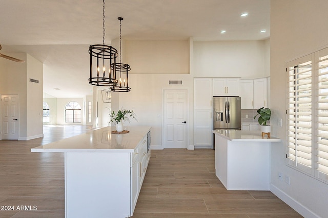 kitchen with a center island, pendant lighting, stainless steel fridge with ice dispenser, white cabinetry, and light hardwood / wood-style flooring