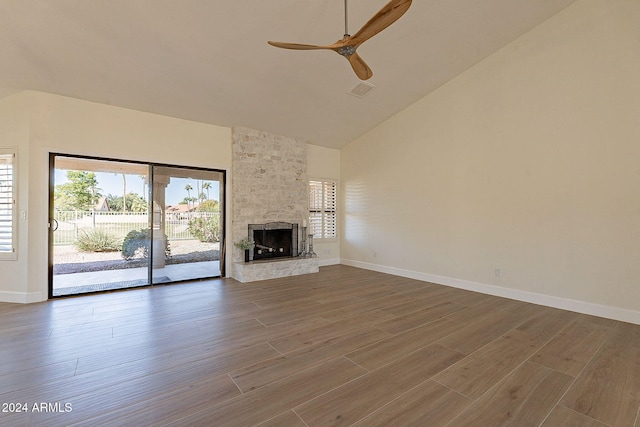 unfurnished living room with hardwood / wood-style floors, ceiling fan, a stone fireplace, and high vaulted ceiling