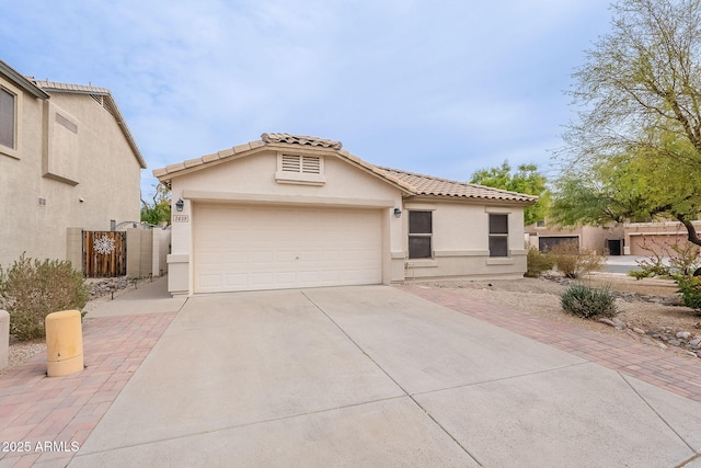 mediterranean / spanish house with a garage, fence, concrete driveway, a tiled roof, and stucco siding