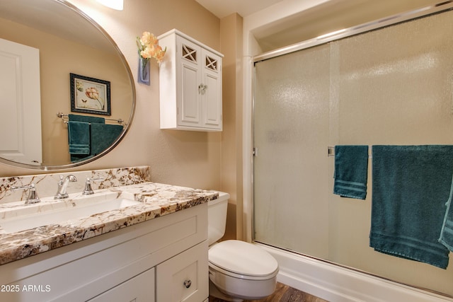 bathroom featuring a shower with door, vanity, and toilet