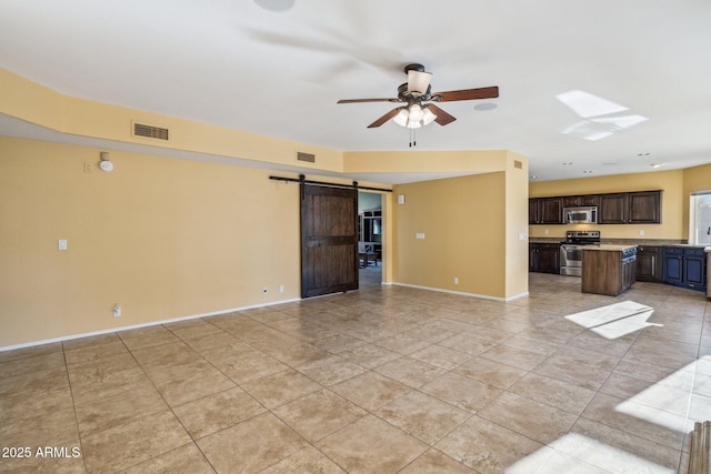 unfurnished living room with a barn door, baseboards, and visible vents