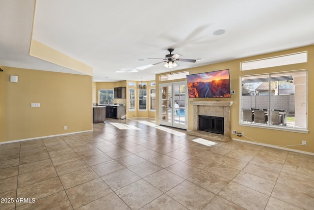 unfurnished living room with light tile patterned floors, a ceiling fan, baseboards, a fireplace with raised hearth, and french doors