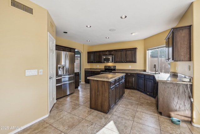 kitchen featuring visible vents, a kitchen island, a sink, stainless steel appliances, and dark brown cabinetry