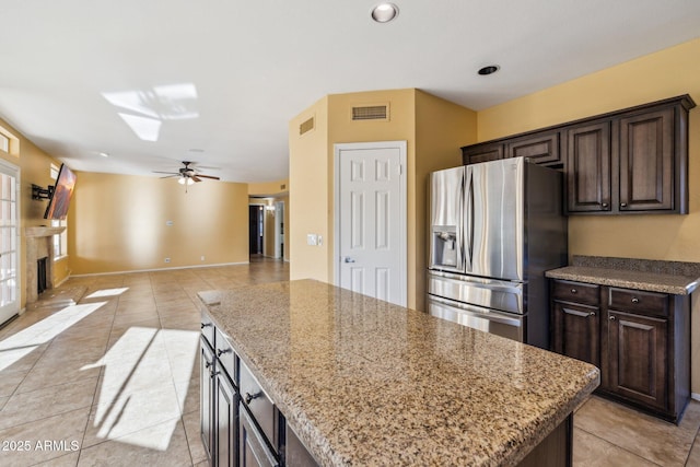 kitchen with a fireplace, stainless steel refrigerator with ice dispenser, light stone countertops, and a center island