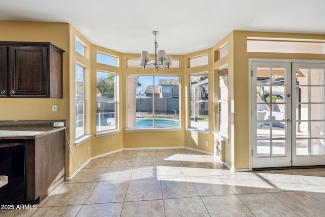 interior space with light tile patterned floors, a notable chandelier, french doors, and baseboards