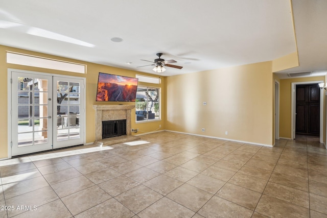 unfurnished living room featuring a fireplace with raised hearth, baseboards, light tile patterned floors, french doors, and a ceiling fan