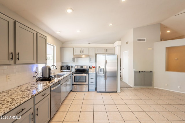 kitchen with appliances with stainless steel finishes, vaulted ceiling, under cabinet range hood, tasteful backsplash, and gray cabinets