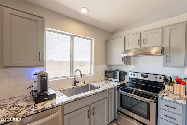 kitchen with stainless steel appliances, under cabinet range hood, a sink, backsplash, and light stone counters