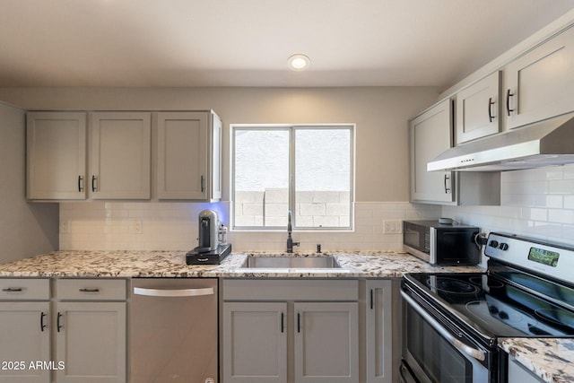 kitchen featuring stainless steel appliances, a sink, under cabinet range hood, gray cabinetry, and backsplash