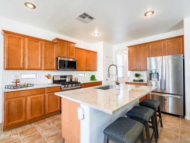 19403 E Arrowhead Trl, Queen Creek, AZ 85142 - kitchen featuring stainless steel appliances, a sink, brown cabinetry, light stone counters, and tasteful backsplash