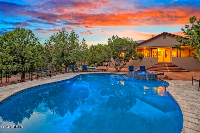 pool at dusk featuring a patio area and an in ground hot tub