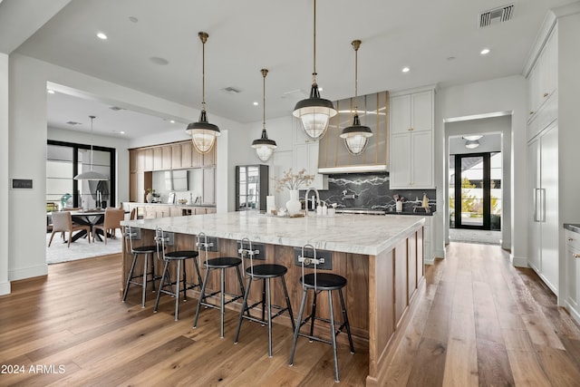 kitchen with light stone countertops, tasteful backsplash, a large island with sink, decorative light fixtures, and white cabinets