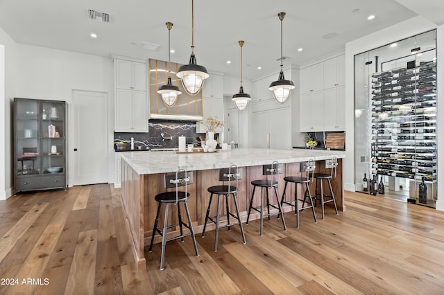 kitchen featuring light stone countertops, white cabinetry, hanging light fixtures, a large island with sink, and light wood-type flooring