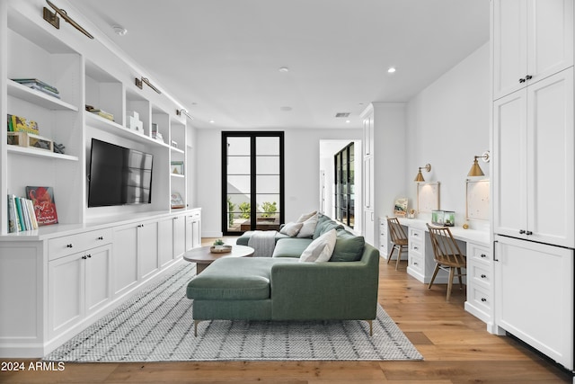 living room featuring built in shelves, built in desk, and light wood-type flooring