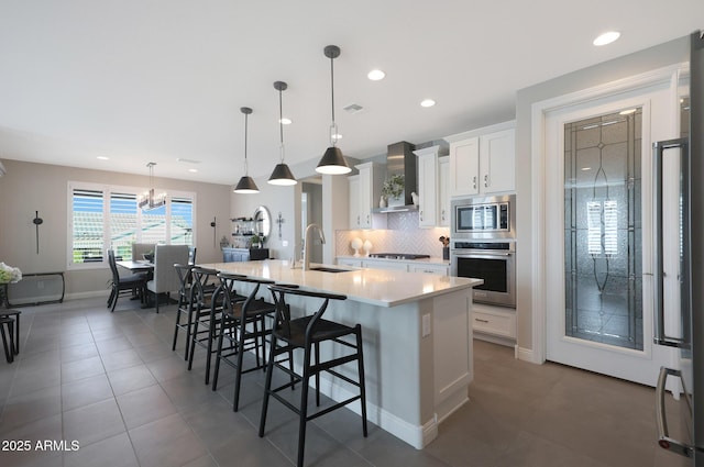 kitchen with tasteful backsplash, wall chimney exhaust hood, appliances with stainless steel finishes, a kitchen island with sink, and a sink