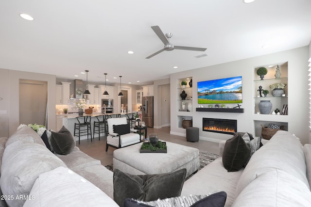 living room with built in features, a glass covered fireplace, visible vents, and recessed lighting