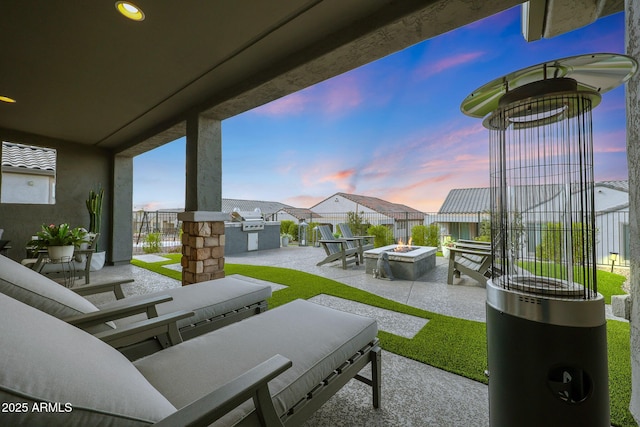 patio terrace at dusk with an outdoor fire pit, area for grilling, fence, and a residential view