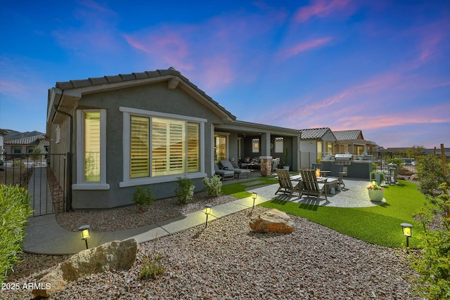 back of property at dusk with a patio area, a yard, fence, and stucco siding