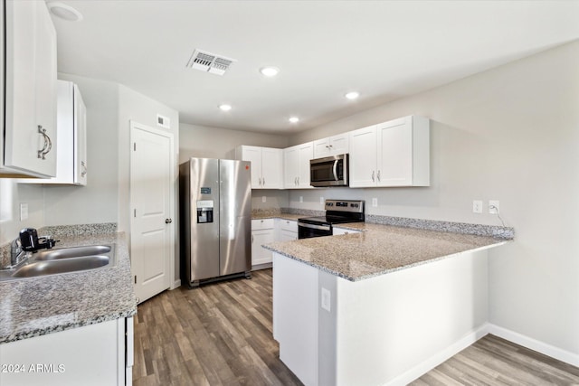 kitchen with kitchen peninsula, appliances with stainless steel finishes, white cabinetry, wood-type flooring, and sink