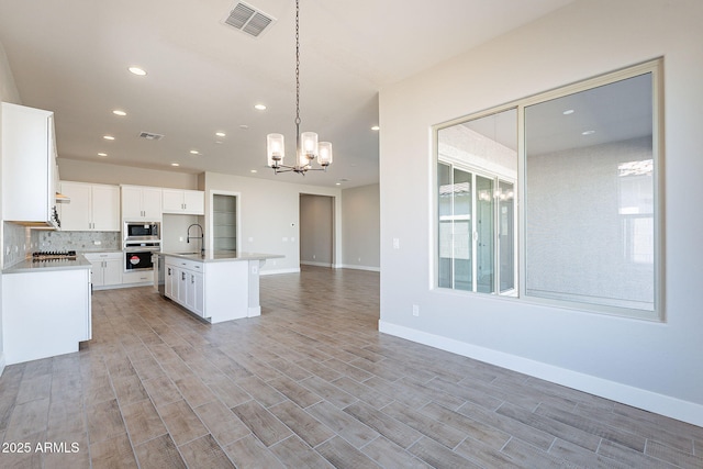 kitchen with a kitchen island with sink, white cabinets, oven, sink, and built in microwave