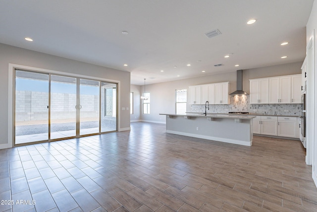 kitchen featuring a center island with sink, oven, sink, wall chimney exhaust hood, and white cabinetry