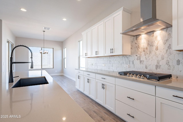 kitchen featuring sink, hanging light fixtures, wall chimney exhaust hood, light hardwood / wood-style floors, and white cabinetry