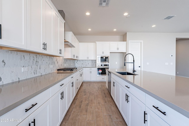 kitchen with sink, light hardwood / wood-style flooring, decorative backsplash, white cabinets, and appliances with stainless steel finishes