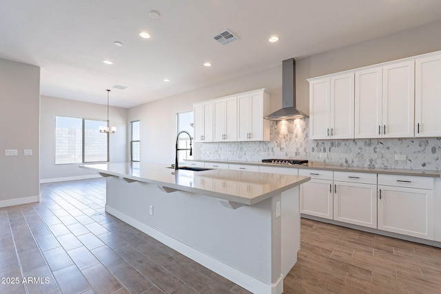 kitchen with wall chimney exhaust hood, sink, and an island with sink