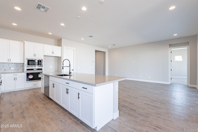 kitchen featuring a kitchen island with sink, sink, tasteful backsplash, white cabinetry, and stainless steel appliances