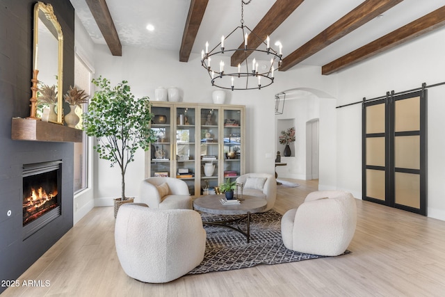 living area with arched walkways, a barn door, light wood-style flooring, a large fireplace, and beamed ceiling