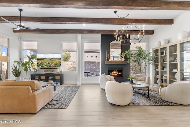 living room with beam ceiling, a notable chandelier, light wood-type flooring, a warm lit fireplace, and baseboards