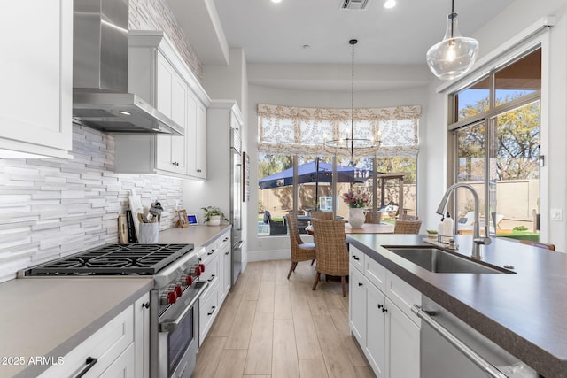 kitchen featuring decorative light fixtures, stainless steel appliances, white cabinetry, a sink, and wall chimney exhaust hood