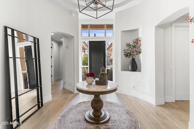 foyer entrance with arched walkways, light wood finished floors, a towering ceiling, and baseboards