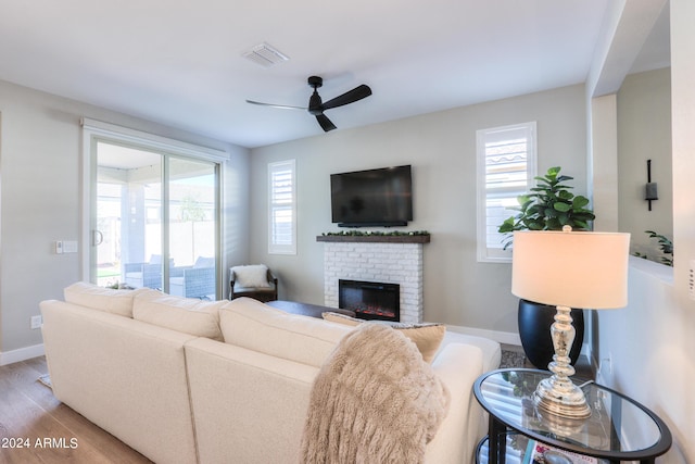 living room with ceiling fan, wood-type flooring, and a brick fireplace