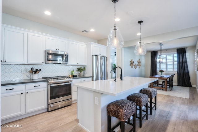 kitchen with white cabinetry, hanging light fixtures, stainless steel appliances, tasteful backsplash, and a kitchen island with sink