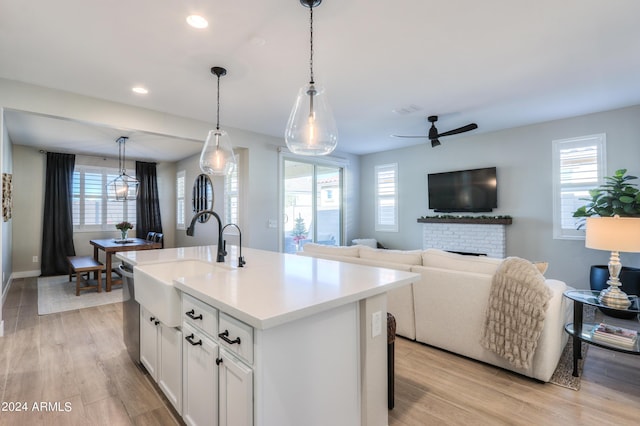 kitchen featuring white cabinetry, sink, hanging light fixtures, a kitchen island with sink, and a fireplace