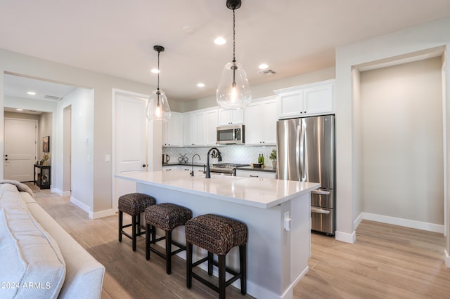 kitchen featuring pendant lighting, stainless steel appliances, white cabinetry, and a kitchen island with sink