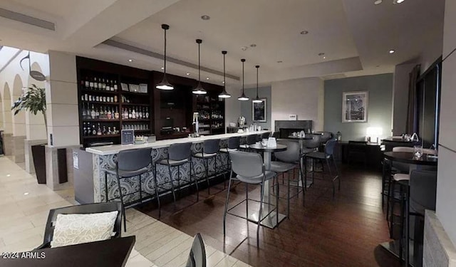 bar featuring a raised ceiling, hanging light fixtures, and hardwood / wood-style flooring