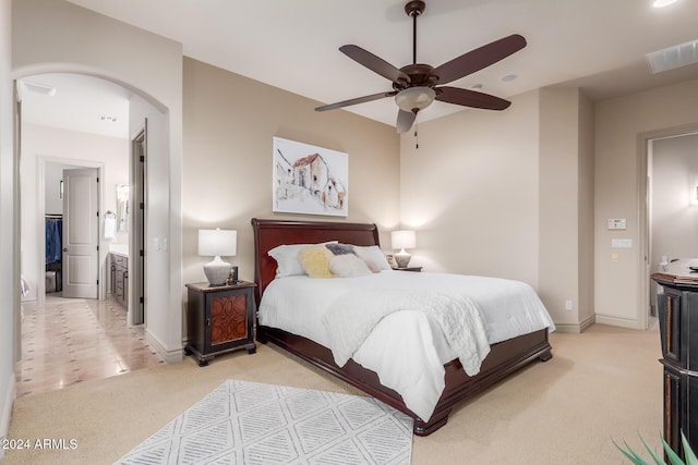 bedroom with ceiling fan, ensuite bathroom, and light carpet